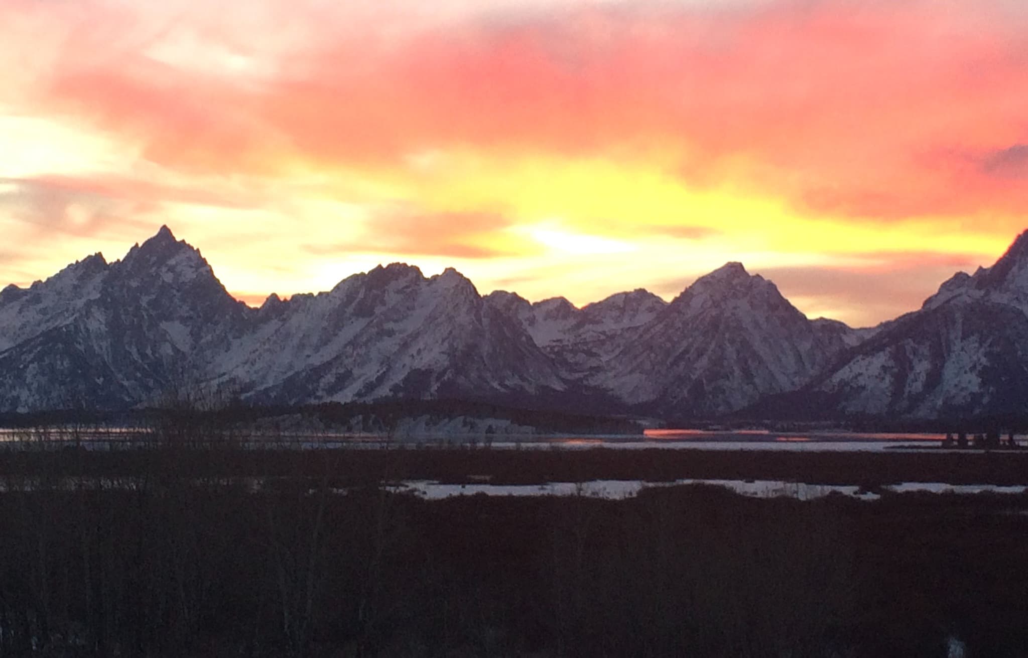 The Teton Range silhouetted against a vivid orange and pink sunset sky